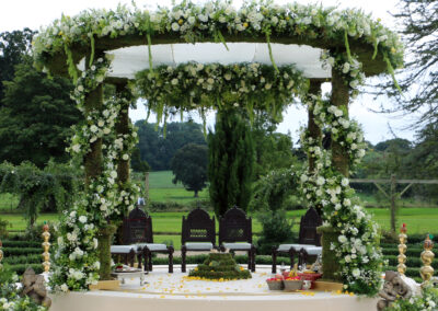 Nishali Moss Mandap with spiral of ENglish styled florals around the pillars and floral border along the top